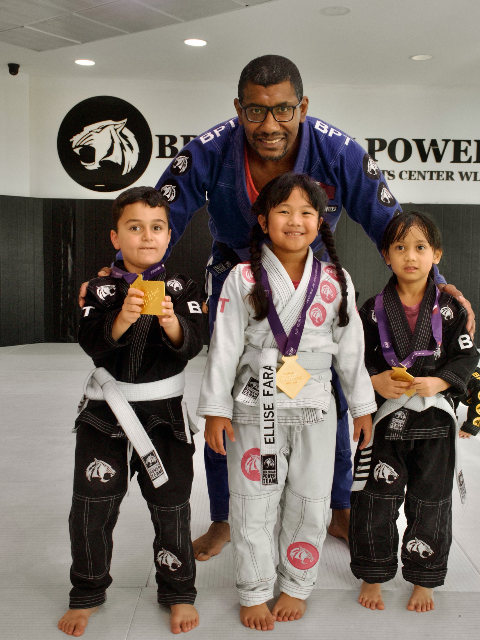 Kids Jiu-Jitsu students holding medals with Coach Marcelo